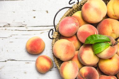 Kırsal beyaz bir masada, sepetin içinde olgun kırmızı şeftaliler, üst manzara. Sağlıklı organik meyve.