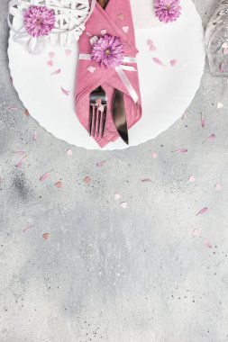 Beautiful festive table setting with white plate, napkin, flowers and hearts decoration on gray stone background. Top view with copy space.