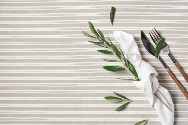 Beautiful flat lay arrangement with cutlery, white napkin and decoration with olive branches. Festive table setting.