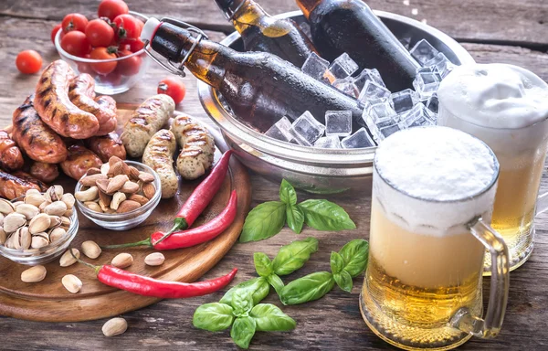 Сосиски на гриле с закусками и кружками пива — стоковое фото