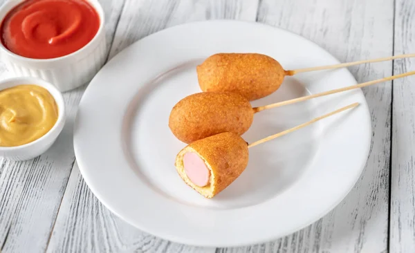 Corn dogs with dip sauces on white serving plate