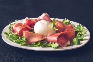 Prosciutto, mozzarella ve servis tabağında taze roka.