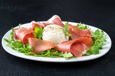 Prosciutto, mozzarella ve servis tabağında taze roka.