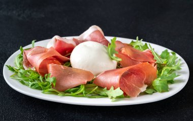 Prosciutto, mozzarella ve servis tabağında taze roka.