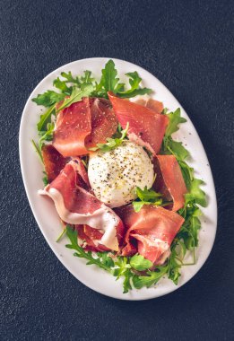 Prosciutto, mozzarella ve servis tabağında taze roka.