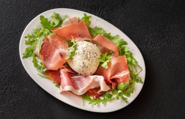 Prosciutto, mozzarella ve servis tabağında taze roka.