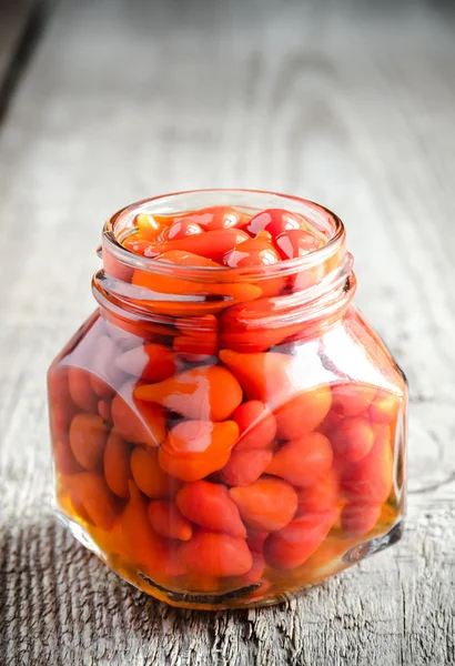 Röd paprika droppar i glasburk på trä bakgrund — Stockfoto