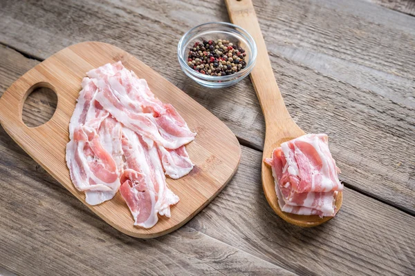 Bacon strips with pepper on wooden spoon — Stock Photo, Image
