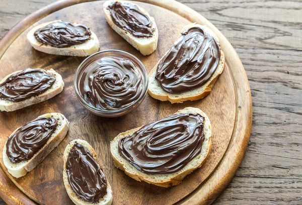 Fette di baguette con crema al cioccolato sulla tavola di legno — Foto Stock
