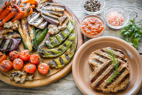 Legumes grelhados com bifes de carne na tábua de madeira — Fotografia de Stock