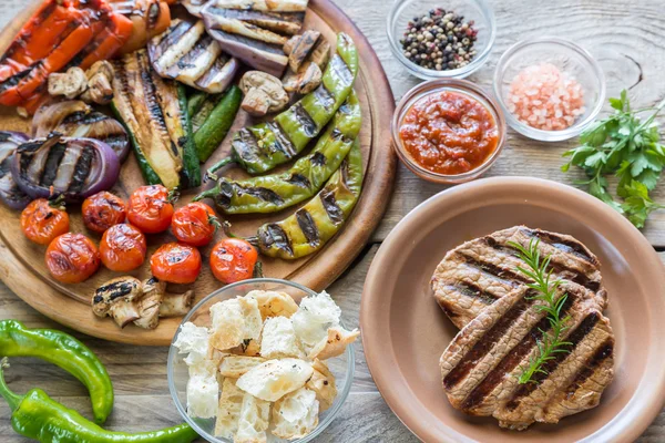 Legumes grelhados com bifes de carne na tábua de madeira — Fotografia de Stock