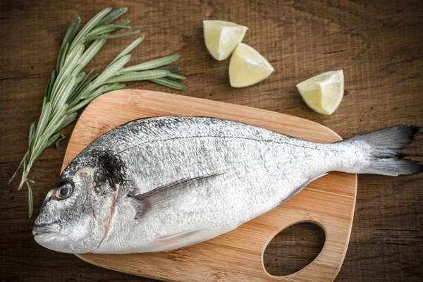 Dorada fresca com ingredientes na tábua de madeira — Fotografia de Stock