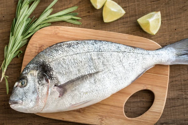 Dorada fresca com ingredientes na tábua de madeira — Fotografia de Stock