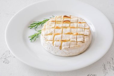 Parlak arka planda erimiş camembert bitkilerinin yer aldığı zarif bir peynir tabağı.