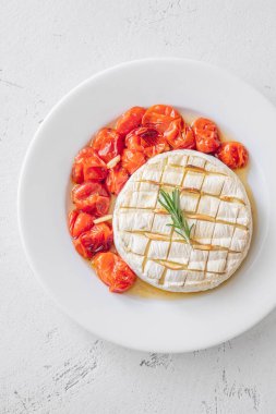 Kremalı fırında peynir, kızarmış ekmek ve parlak beyaz arka planda sulu domateslerle servis edilir.