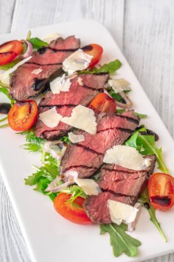 Peynir ve domatesli orta pişmiş biftek dilimleri, restoran tarzı sunum, temiz arka plan.