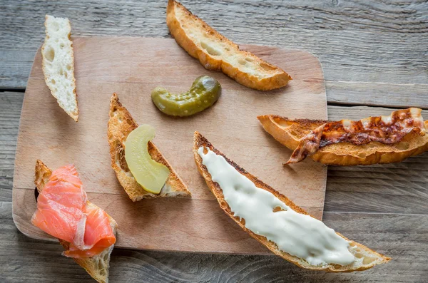 Pane tostato con diversi condimenti sulla tavola di legno — Foto Stock