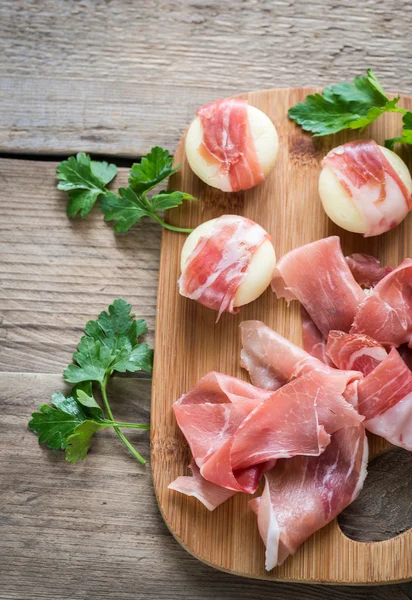 Mini cheese and prosciutto wraps on the wooden board — Stock Photo, Image