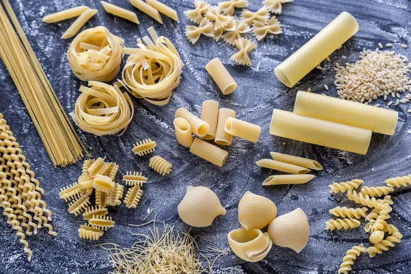 Vários tipos de macarrão no fundo de poeira de farinha escura — Fotografia de Stock