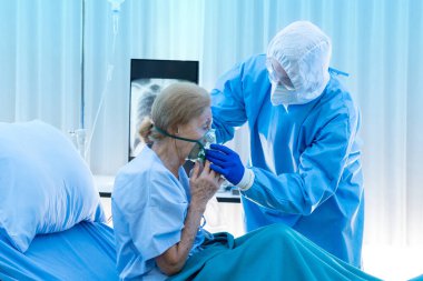 Tıbbi ekip karantina odasındaki yaşlı hastaya oksijen maskesi veriyor. Beyaz kadınlar yasak bölgelerde akciğer enfeksiyonundan muzdaripler. Koronavirüs 2019-2020 küresel salgınının bir parçası.