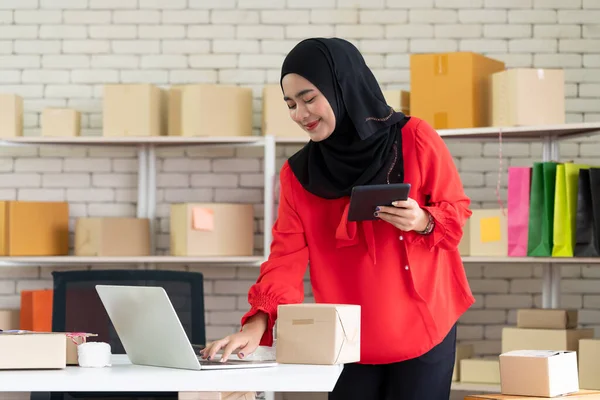 Genç Girişimci Girişimci, Bayan Müslüman satıcı bir müşteriden sipariş almak ve doğrulamak için tabletle dizüstü bilgisayar kullanıyor. E-ticaret konsepti online alışveriş, evden küçük teslimat işi.