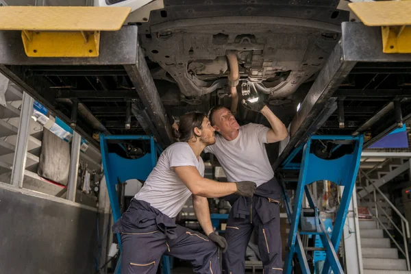 Beyaz araba tamircisi ve otomotiv ekibi lastik dükkanındaki süspansiyon sistemi parçalarını kontrol etmek için meşale kullanıyor. Garaj atölyesinde profesyonel araba tamircisi. Servisi otomatik onar