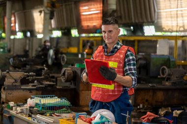 Endüstriyel fabrikada çalışırken elinde kalem ve dosya tutan düşünceli beyaz işçinin portresi. Profesyonel mühendis, kendi çalışma programını atölyede düşünüyor..