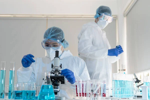 Kadın bilim adamları kovid 19 virüs aşısını tıbbi bir laboratuvarda araştırmak için mikroskop kullanıyorlar. Bir doktor kimya laboratuvarında koronavirüsü araştırmak için biyoteknoloji kullanır. İlaç bilimi kavramları.
