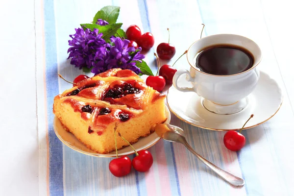 Slice of cherry pie on a plate with cherriesand tea cup in background — Stock Photo, Image