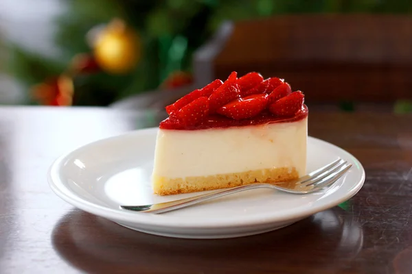 Tarta de queso fresa fresca. Enfoque selectivo en el borde superior frontal de la torta. Árbol de Navidad en segundo plano — Foto de Stock