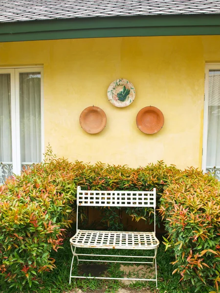 Metal bench in a garden on yellow wall background — Stock Photo, Image