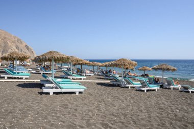 Santorini, Yunanistan - 17 Eylül 2020: Santorini adasındaki Perissa 'nın siyah volkanik kumlu plajında güneşleniyor. Cyclades, Yunanistan