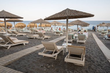 Santorini, Yunanistan - 18 Eylül 2020: Santorini 'deki siyah volkanik kum plajındaki güneş pansiyonları. Cyclades, Yunanistan