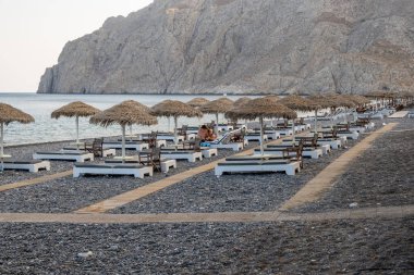 Santorini, Yunanistan - 18 Eylül 2020: Santorini 'deki siyah volkanik kum plajındaki güneş pansiyonları. Cyclades, Yunanistan