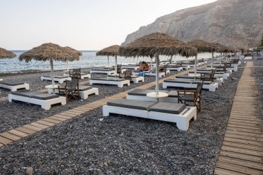 Santorini, Yunanistan - 18 Eylül 2020: Santorini 'deki siyah volkanik kum plajındaki güneş pansiyonları. Cyclades, Yunanistan