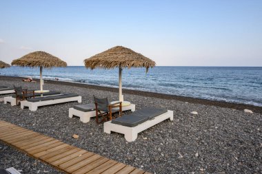 Santorini, Yunanistan - 18 Eylül 2020: Santorini 'deki siyah volkanik kum plajındaki güneş pansiyonları. Cyclades, Yunanistan