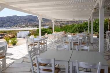 Ios, Yunanistan - 21 Eylül 2020: Ios Adası 'ndaki Manganari plajındaki Yunan restoranında masa ve sandalyeler. Cyclades, Yunanistan