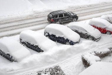 Şehir caddesindeki otoparkta kar arabaları kapladı. Karla kaplı bir yolda giden bir araba. Kış mevsimi