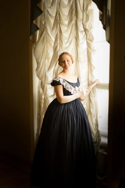 Young woman in long ball dress standing at the window at the ball — Stock Photo, Image