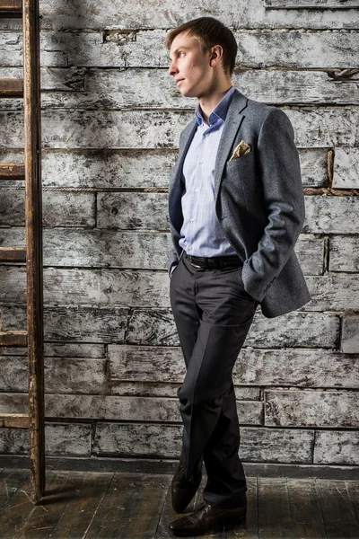 Un hombre joven con un traje de negocios gris y una camisa ligera de pie en toda su longitud en el estudio de rodaje — Foto de Stock