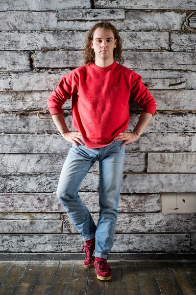 Молодой человек в красном свитере и джинсах сидит на деревянном стуле — стоковое фото