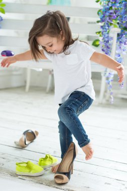 Beyaz T-shirt ve jeans oynama ve annesinin yüksek topuklar üzerinde çalışırken, küçük kız