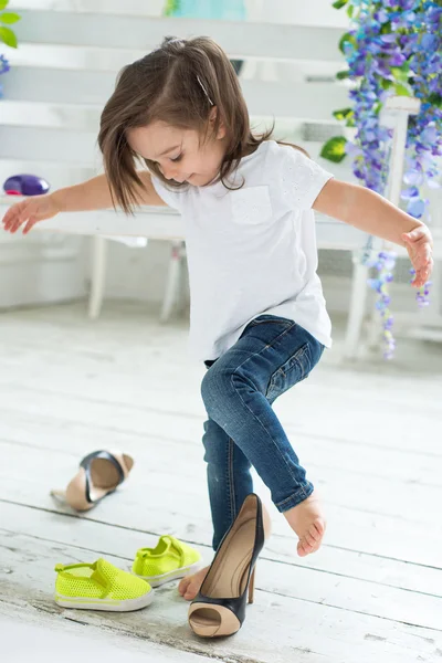 Beyaz T-shirt ve jeans oynama ve annesinin yüksek topuklar üzerinde çalışırken, küçük kız