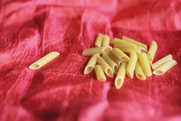 Κίτρινο ζυμαρικά διάσπαρτα στο τραπέζι σε κόκκινο φόντο — Φωτογραφία Αρχείου