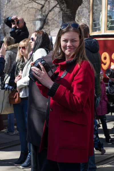 The girl with the camera in a red coat among people — Stock Photo, Image