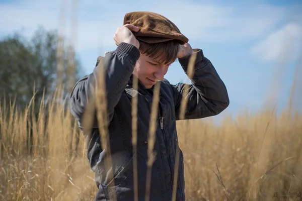 Agronomo giovane uomo in un maglione marrone e cappello cammina sul campo — Foto Stock