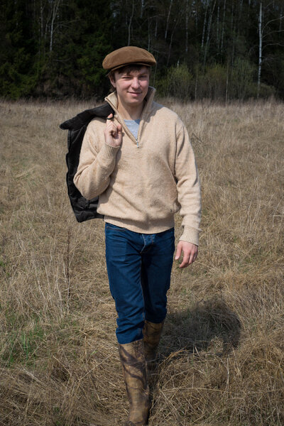 Agronomist  young man in a brown sweater and cap walks on the field