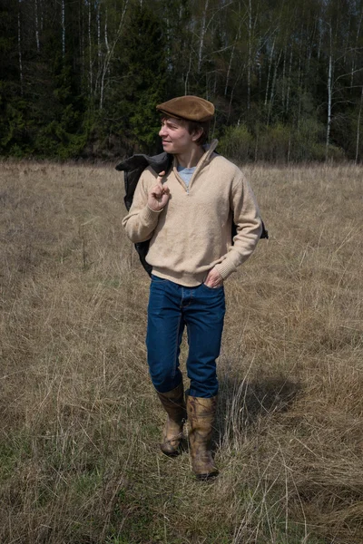 A young man  in a brown sweater and cap walks on the field — Stock Photo, Image