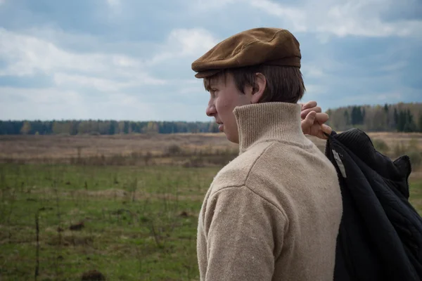 Un giovane uomo in un maglione marrone e cappello cammina sul campo — Foto Stock