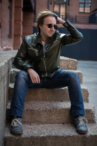 Jonge man in zonnebril en een leren jas zittend op stenen trap — Stockfoto